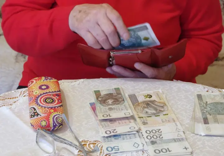 Dłonie chowają banknot 100 zł do czerwonego portfela. Obok leżą pieniądze, okulary i etui. To pokazuje, gdzie trzymać pieniądze.