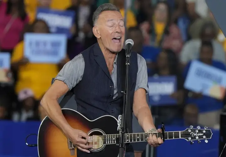 Bruce Springsteen sjunger och spelar gitarr på scenen. Publiken håller upp skyltar, vilket antyder ett kommande evenemang med Bruce Springsteen.