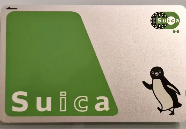 Eine Suica-Karte mit einem fröhlichen Pinguin-Motiv. Die Karte ist silberfarben mit einem großen grünen Feld und dem Schriftzug "Suica".