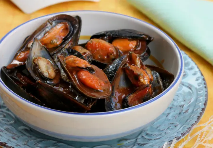 Un invitante sautè di cozze, succulente e profumate, servite in una ciotola bianca con bordo blu.