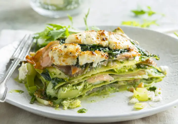 Une part de lasagne saumon épinard, gratinée au fromage, servie avec une salade verte.