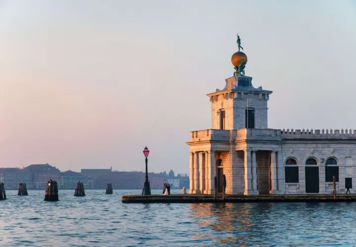 La Dogana di Venezia, un bâtiment historique, se dresse au bord de l'eau. Un couple s'embrasse près d'un lampadaire.