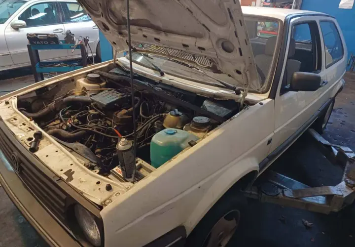 Biały Volkswagen Golf z otwartą maską, silnik gotowy do wyjęcia. Zastanawiasz się, ile kosztuje wyciągnięcie silnika?