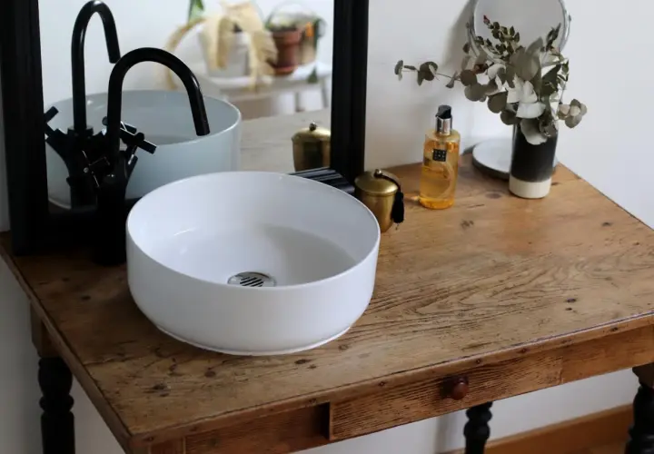 Un plan pour créer son meuble de salle de bain : vasque blanche, robinetterie noire, miroir et accessoires déco sur un meuble ancien.