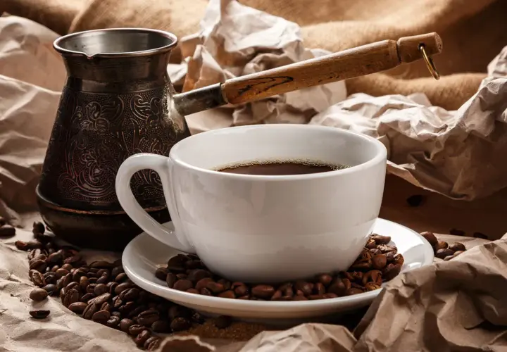 Ein traditioneller Mokkakanne und eine Tasse mit griechischem Mokka, umgeben von Kaffeebohnen und zerknülltem Papier.