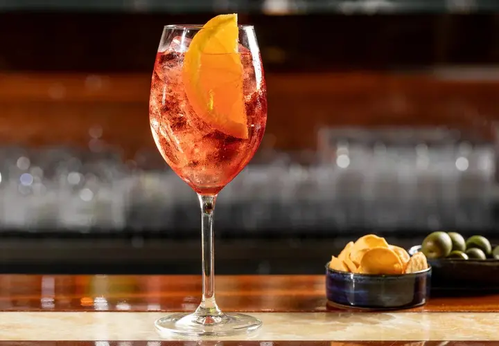 Un bicchiere di Aperol Spritz, rinfrescante e colorato, pronto per un aperitivo con patatine e olive.