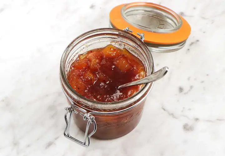 En burk med hemlagad mango chutney, perfekt för ditt nästa mango chutney recept. En sked vilar i den söta, kryddiga blandningen.