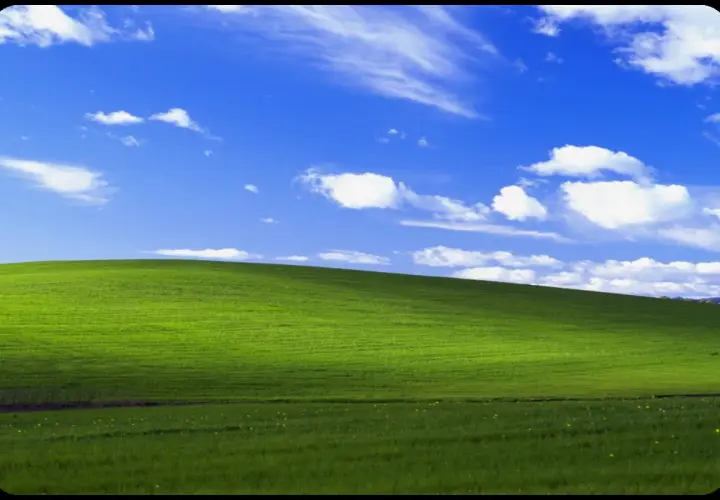 Zielone wzgórze pod błękitnym niebem z chmurami, ikoniczny widok z **win xp virtual machine**.