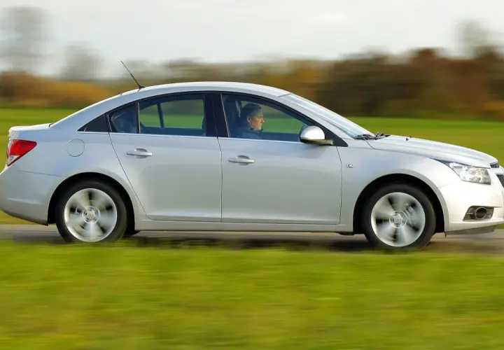 Srebrny Chevrolet Cruze 1.8 benzyna w ruchu, z kierowcą za kierownicą, przemierza wiejską drogę pośród zielonych pól.