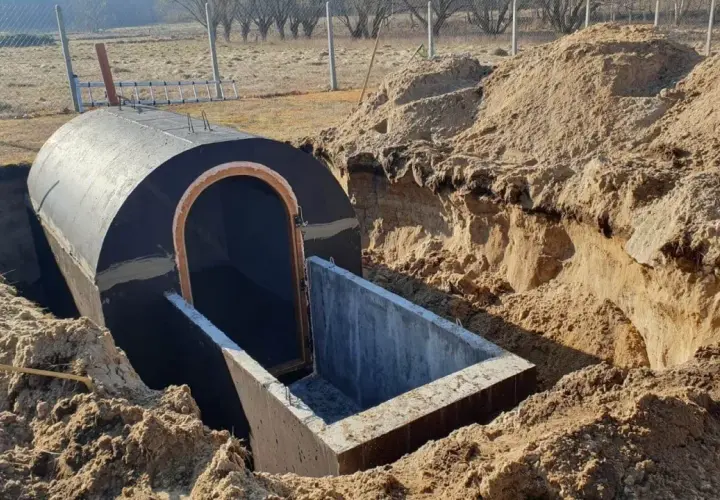 Budowa piwnicy ziemianki w trakcie. Okrągły, betonowy tunel z wejściem wkopany w ziemię, otoczony usypanym piaskiem.