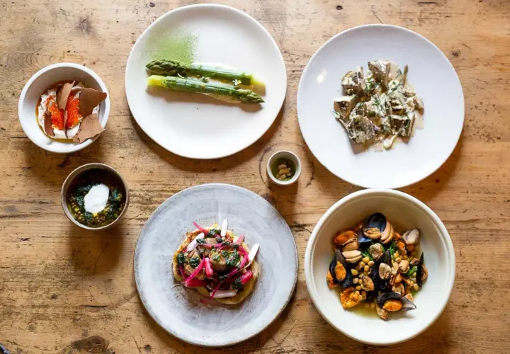 Assortiment de plats gastronomiques : asperges, moules, tartare, et autres mets fins sur table en bois.