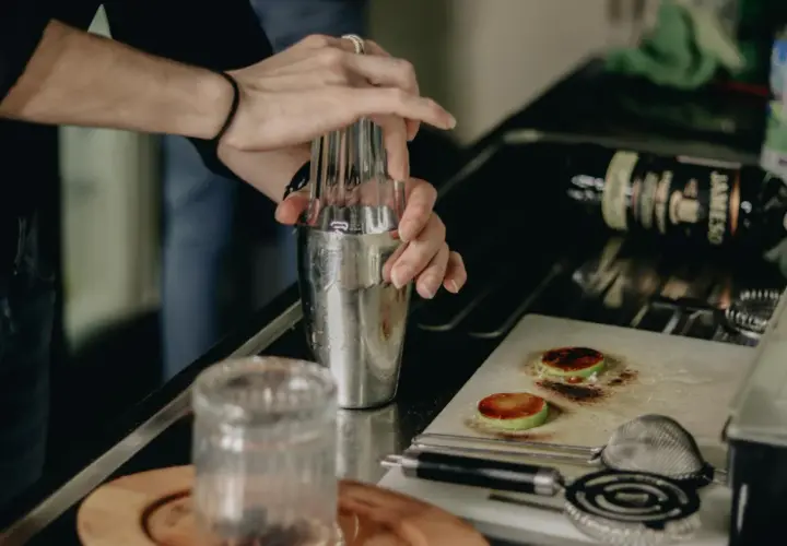 Ręce barmana mieszają składniki w shakerze, by uzyskać idealne rozcieńczenie. Na blacie leży butelka whisky.