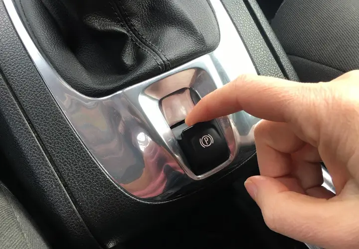 Dito, un dito preme il pulsante del freno a mano automatico, un gesto comune per parcheggiare in sicurezza.