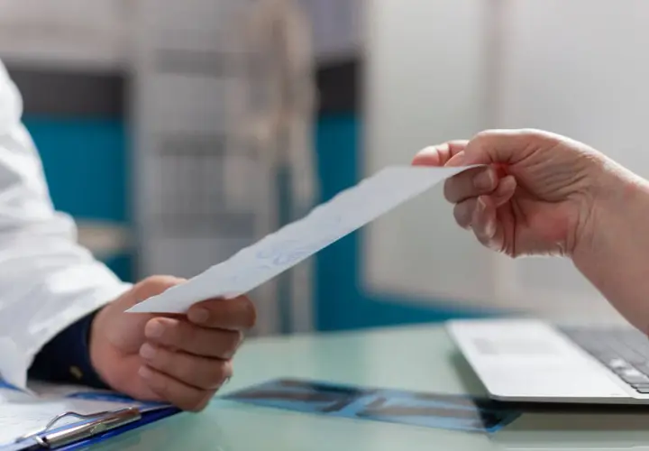 Lekarz przekazuje pacjentowi dokument, prawdopodobnie wniosek o świadczenie rehabilitacyjne.