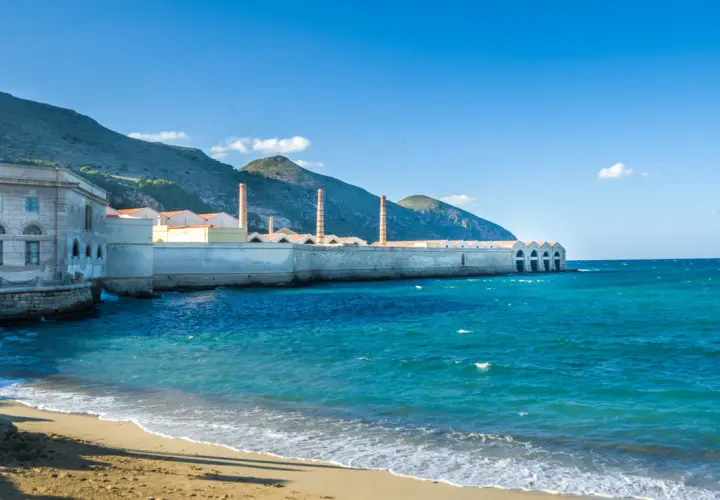 Ancienne conserverie de thon à Favignana, Sicile, avec ses cheminées emblématiques se dressant face à la mer turquoise.