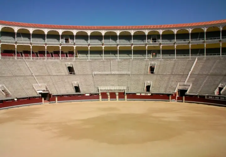 Vista interior de una plaza de toros vacía, con gradas de piedra y balcones arqueados. Las ventas por dentro esperan al público.