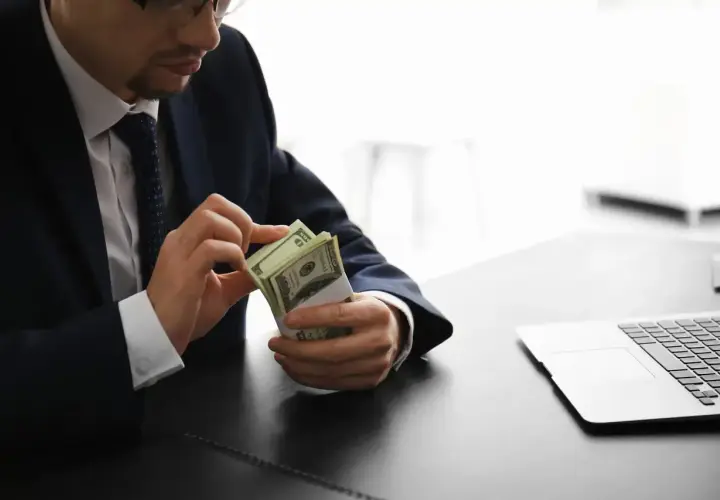 Mężczyzna w garniturze liczy banknoty dolarowe przy biurku. Jego praca w banku wymaga precyzji.