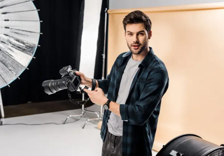 Młody fotograf z aparatem w studio. Chcesz wiedzieć, jak napisać opinie dla fotografa? Oto wskazówki!