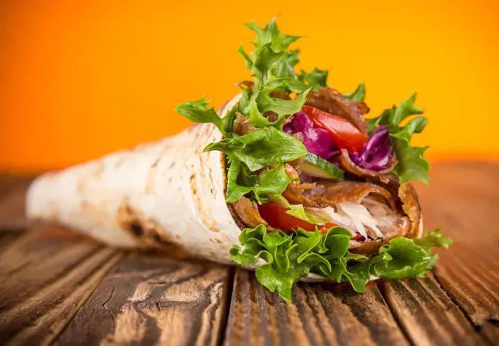 Kebab zawinięty w placek z mięsem, warzywami i sałatą na drewnianym stole.