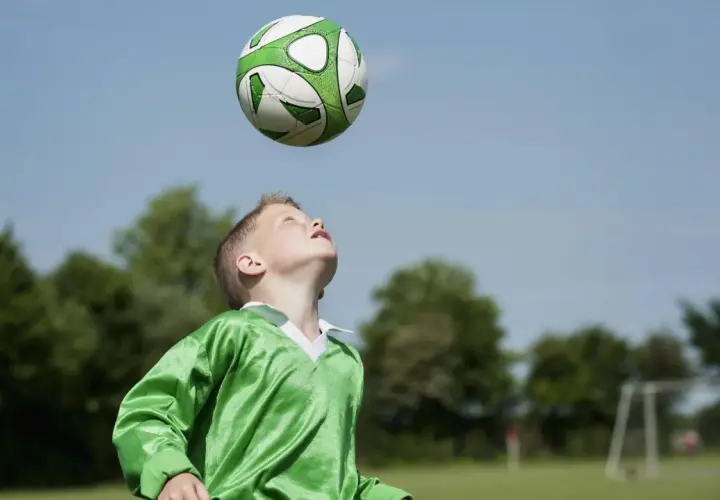 Junge im grünen Trikot übt den Kopfball. Der Ball schwebt über ihm, bereit für den perfekten Treffer.