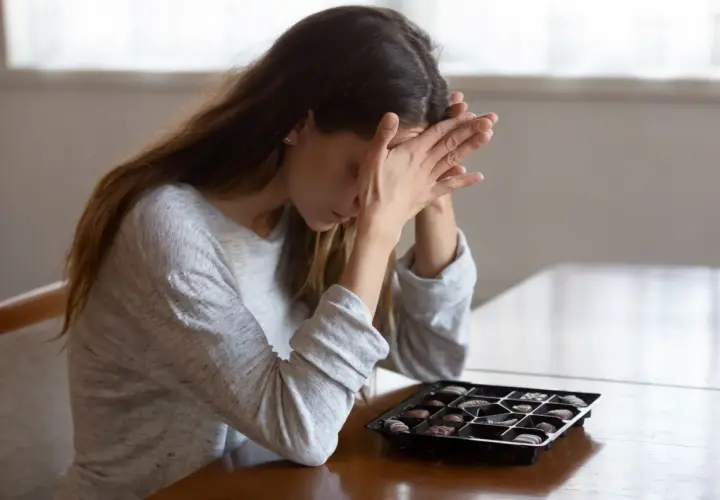 Donna con le mani sul viso, davanti a una scatola di cioccolatini, forse cercando un antidepressivo naturale più potente.