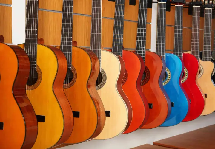 Rząd gitar klasycznych i akustycznych w różnych kolorach. Różnice między nimi to m.in. struny i pudło rezonansowe.