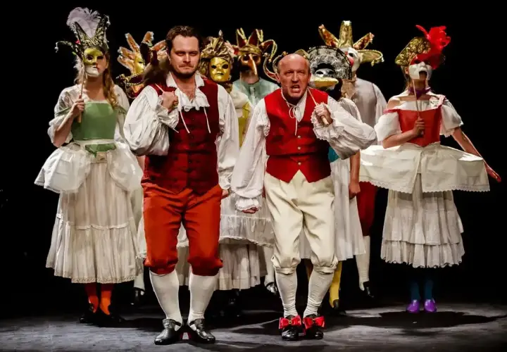Aktorzy w barwnych strojach i maskach na scenie Teatru im. Jaracza w Warszawie.
