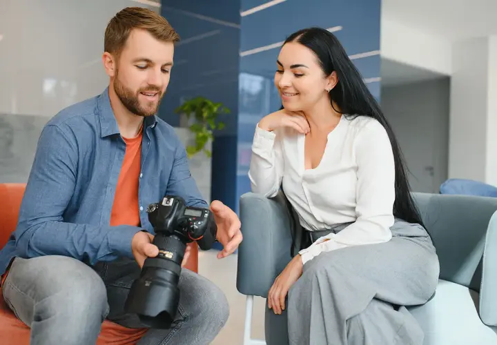 Mężczyzna z aparatem pokazuje kobiecie efekty swojej pracy. Fotograf omawia szczegóły sesji.