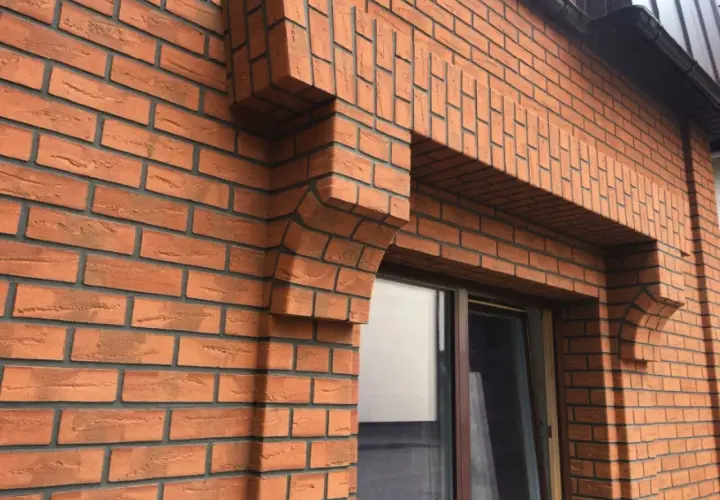Fragment elewacji z cegły klinkierowej z ozdobnym gzymsem nad oknem.