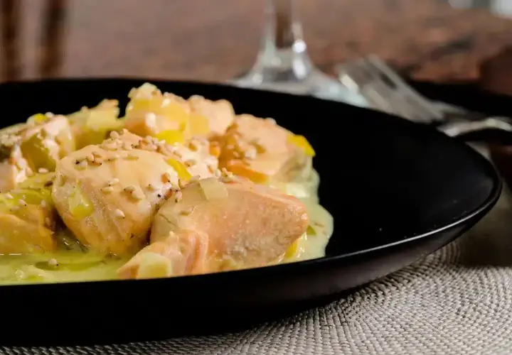 Délicieuse blanquette de saumon au vin blanc, parsemée de graines de sésame, servie dans une assiette noire.