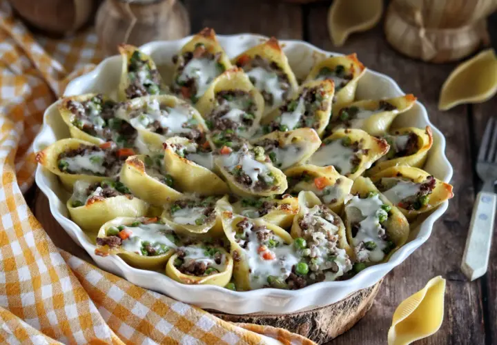 Conchiglioni à la sicilienne, pâtes farcies à la viande et aux petits pois, gratinées au fromage fondant dans un plat blanc.