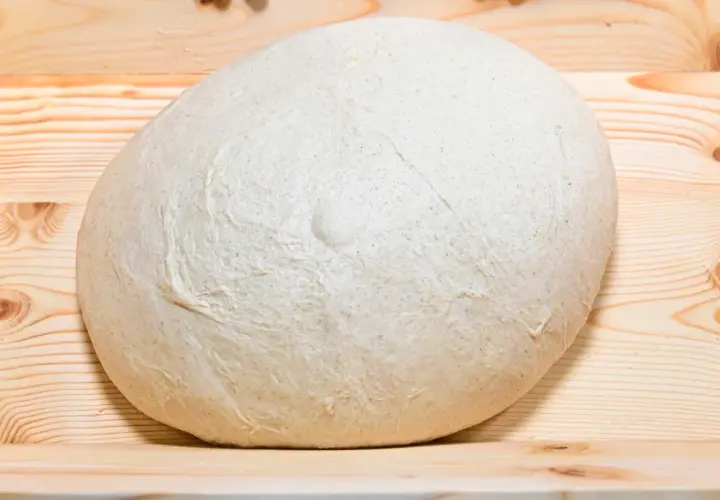 Impasto lievitato per pizza in casa, pronto per essere steso su un tagliere di legno.