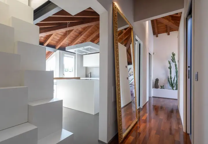 Specchio dorato e cactus per rendere luminoso un corridoio moderno con soffitto a vista in legno.