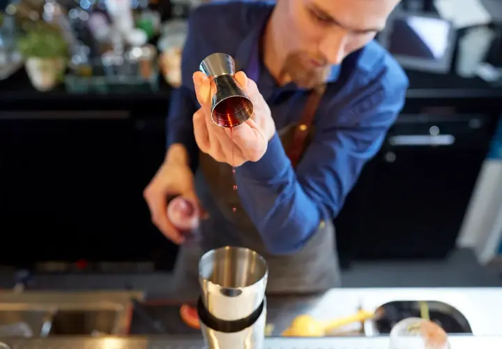 Barman przelewa czerwony płyn z jiggera do shakera.