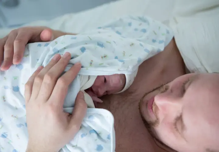 Ciepłe kangurowanie przez tatę po cesarce. Maluszek wtulony w klatkę piersiową ojca, czuje jego bicie serca.