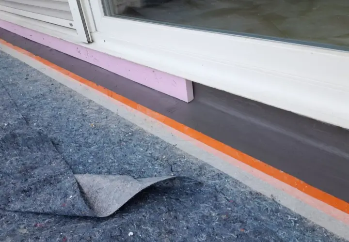 Schutzmatte liegt bereit, um den Sockel abzudichten. Dämmung und Abdichtung am Fenster sind sichtbar.