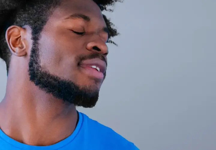 Hombre con ojos cerrados y barba cuidada, parece disfrutar de un momento de paz. Sus perillas resaltan su rostro.