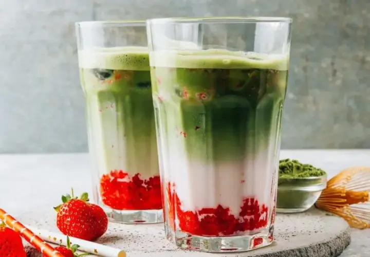 Zwei erfrischende Matcha-Erdbeer-Latte-Gläser mit Schichten aus Erdbeeren, Milch und leuchtend grünem Matcha.