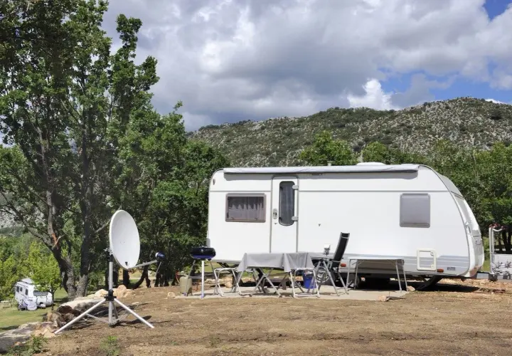 Schéma installation TV camping-car : parabole satellite devant une caravane, avec table et chaises dressées pour un repas en plein air.