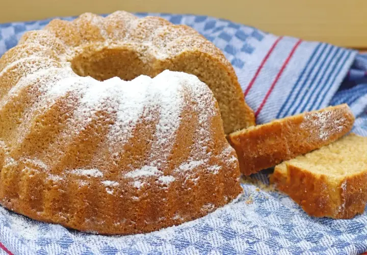 Puszysta babka panettone, oprószona cukrem pudrem, leży na niebiesko-białym ręczniku. Obok niej leżą dwa kawałki ciasta.