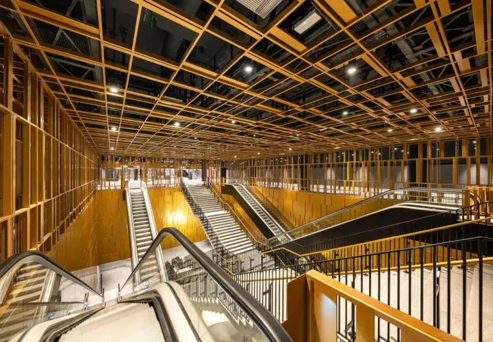 Interni moderni di una stazione metro con soffitto a griglia dorata, scale mobili e gradinate. Un assaggio delle future metro c fermate.