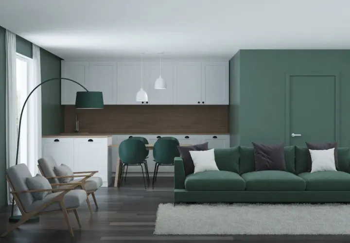 Nowoczesny salon z kuchnią, gdzie króluje **zielony kolor ścian**. Wygodna kanapa, fotele i krzesła tworzą przytulną przestrzeń.