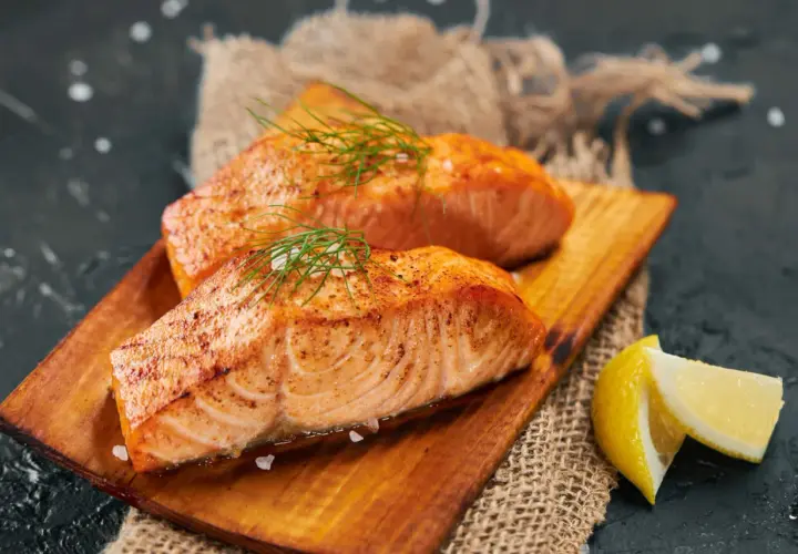 Deux pavés de saumon grillé, parsemés d'aneth et de gros sel, servis sur une planche en bois avec des quartiers de citron. Un délice pour accompagner un bon vin.