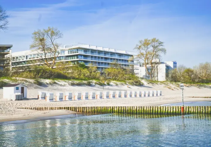 Nowoczesny seaside park hotel z widokiem na plażę i morze. Rząd białych leżaków plażowych czeka na gości.