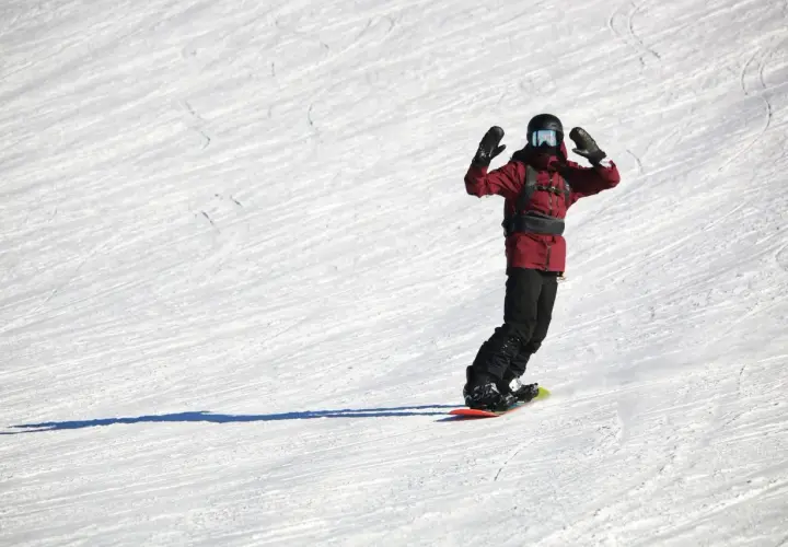 Snowboardzista w czerwonej kurtce z rękami w górze na ośnieżonym stoku.