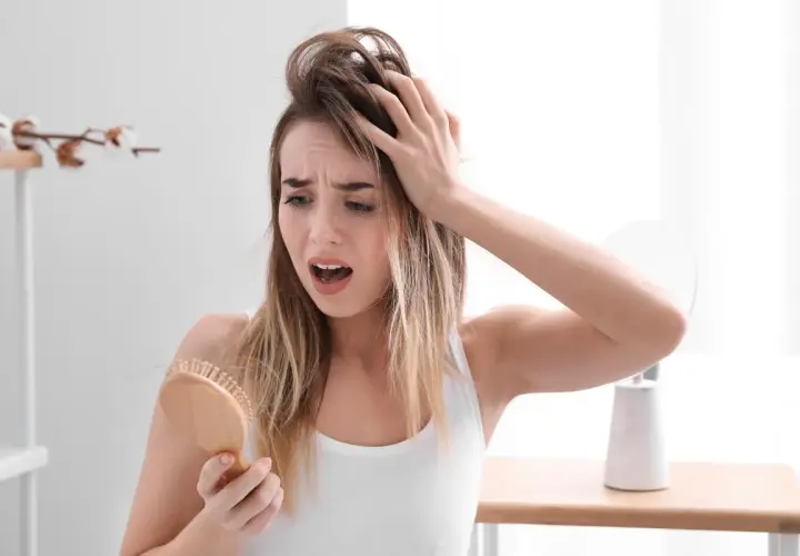 Mujer preocupada por la caida de pelo en verano, con mechones en el cepillo.