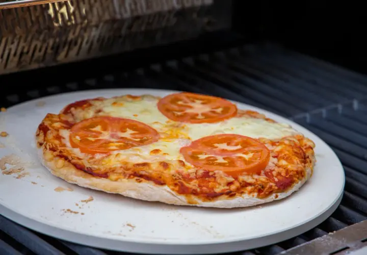 Eine Margherita-Pizza mit Tomatenscheiben und geschmolzenem Käse wird auf einem Pizzastein im Backofen gebacken.