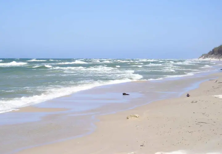 Plaża w Rowach, z falującym morzem i piaszczystym brzegiem. W oddali widać wydmy i nielicznych spacerowiczów.