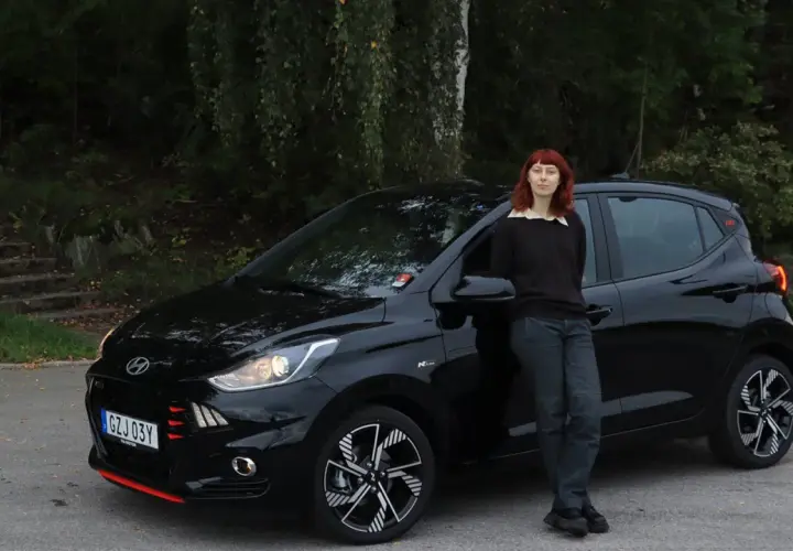 En kvinna med rött hår lutar sig mot en svart Hyundai i10. Bilen är redo för ett test.