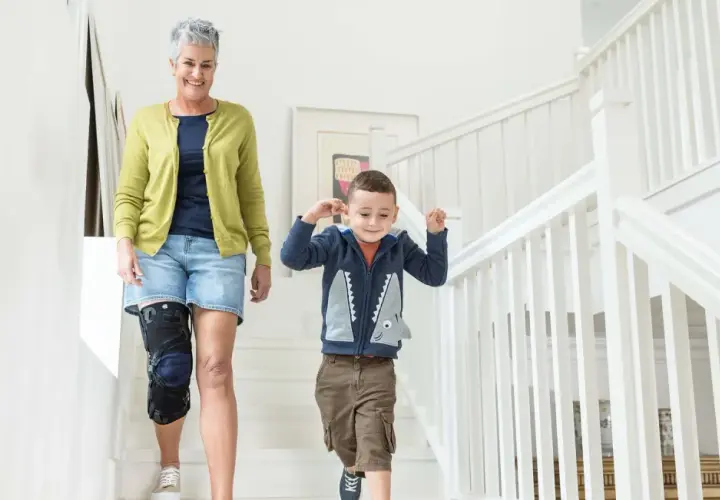Frau mit Kniebandage, die mit ihrem Enkel die Treppe hinuntergeht. Einlagen bei Kniearthrose können helfen, die Mobilität zu verbessern.